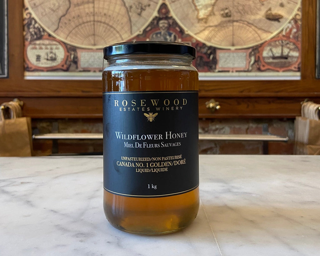 A 1 kg glass jar of Rosewood Estate Winery Wildflower Honey sits on a white marble countertop, with a vintage world map hanging on the wooden wall behind it.